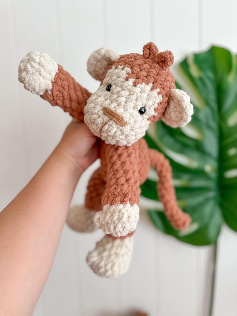 Peut inclure: Une peluche singe au crochet faite &agrave; la main, dans des tons de marron et de cr&egrave;me. Le singe a un aspect textur&eacute; et doux avec une longue queue et des bras tendus. Le visage du jouet pr&eacute;sente de petits yeux noirs et un nez beige.