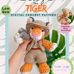 May include: A digital crochet pattern for a tiger plushie named Blaze, wearing a safari outfit. The plushie is orange, white, and tan, with a pink nose and a hat. The image includes the text "Cheetah Mod Included" and "Timeless Plushie Collection."