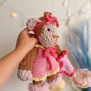 Peut inclure: Poup&eacute;e singe au crochet faite &agrave; la main, avec une robe, un n&oelig;ud et des bottes roses. La poup&eacute;e a une fourrure marron et beige, un n&oelig;ud rose sur la t&ecirc;te et des accents jaunes sur la robe et les bottes. La poup&eacute;e mesure environ 25 cm de haut.