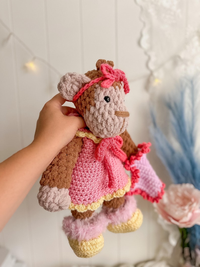 Peut inclure: Poup&eacute;e singe au crochet faite &agrave; la main, avec une robe, un n&oelig;ud et des bottes roses. La poup&eacute;e a une fourrure marron et beige, un n&oelig;ud rose sur la t&ecirc;te et des accents jaunes sur la robe et les bottes. La poup&eacute;e mesure environ 25 cm de haut.