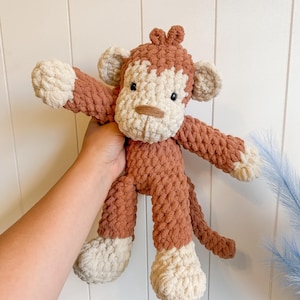 Peut inclure: Un singe en crochet fait &agrave; la main, de couleur marron et cr&egrave;me. Le jouet en peluche pr&eacute;sente un visage d&eacute;taill&eacute;, des bras, des jambes et une queue. Le corps du singe est brun chaud, avec des accents cr&egrave;me sur le visage, les mains et les pieds.