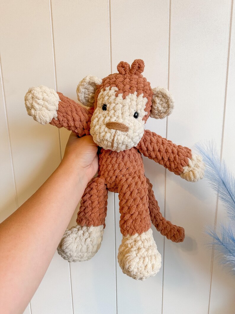 Peut inclure: Un singe en crochet fait &agrave; la main, de couleur marron et cr&egrave;me. Le jouet en peluche pr&eacute;sente un visage d&eacute;taill&eacute;, des bras, des jambes et une queue. Le corps du singe est brun chaud, avec des accents cr&egrave;me sur le visage, les mains et les pieds.