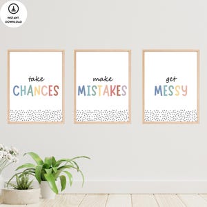 Op de afbeelding: Drie ingelijste prints met een witte achtergrond en zwarte stippen aan de onderkant. De prints hebben kleurrijke tekst die "kansen grijpen", "fouten maken" en "rommel maken" luidt.