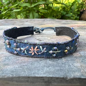 Handbroderat sidenarmband med ädelstenspärlor. Handgjort av handfärgad bomull och återvunnet sari-sidensband och läderbaksida.