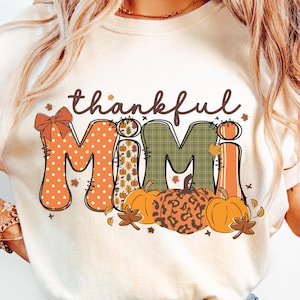 May include: Cream-colored t-shirt with the words "thankful MIMI" in a fall-themed design. The word "MIMI" is decorated with polka dots, pumpkins, and fall leaves. Pumpkins and leaves are at the bottom of the design.