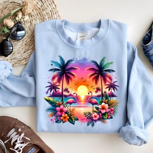 May include: A light blue sweatshirt with a colorful sunset scene featuring palm trees, pink flamingos, and tropical flowers.