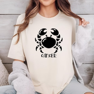 May include: A white t-shirt with a black graphic of a crab and the word "Cancer" underneath.