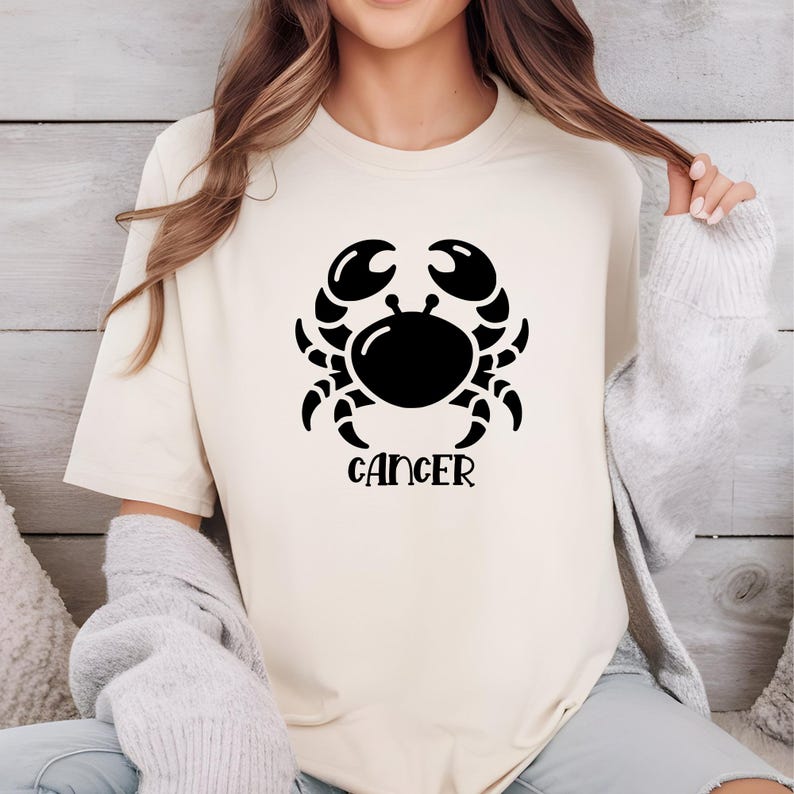 May include: A white t-shirt with a black graphic of a crab and the word "Cancer" underneath.