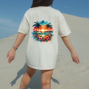 Pu&ograve; includere: Una maglietta bianca con una stampa grafica colorata di una scena di tramonto tropicale con palme, fiori e una spiaggia.