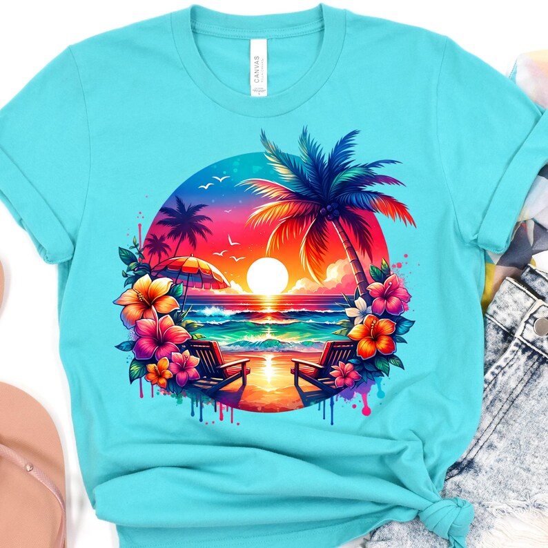 May include: A light blue t-shirt featuring a vibrant beach scene. The graphic includes a sunset over the ocean, palm trees, beach chairs, and colorful flowers. The word "Canvas" is printed on the upper left side of the shirt.