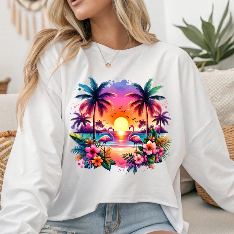 May include: White long-sleeved shirt with a colorful graphic print of palm trees, flamingos, and a sunset. The graphic is surrounded by pink and purple flowers.