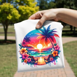 May include: White t-shirt featuring a vibrant beach scene. The design includes a sunset, palm trees, ocean waves, and colorful flowers. Two beach chairs are positioned on the sand. The artwork is enclosed in a circular frame.
