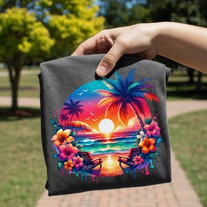 May include: Dark gray t-shirt featuring a vibrant beach scene. The design includes a sunset, palm trees, beach chairs, and colorful flowers. The artwork is framed in a circular shape, with a bright, tropical color palette.