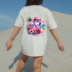 May include: A white t-shirt with a pink flamingo wearing sunglasses and surrounded by tropical flowers and a beach scene.