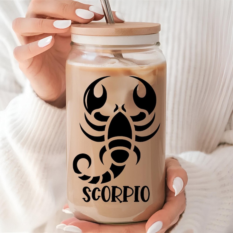 May include: A clear glass reusable iced coffee tumbler with a brown bamboo lid. The tumbler features a black silhouette of a scorpion with the word "SCORPIO" printed below it.