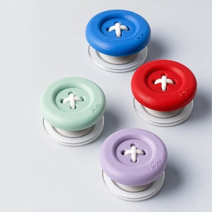 May include: Four circular button-shaped objects in blue, red, light green, and light purple. Each features a central indentation with white thread stitched in a cross pattern. The word pips is embossed on the side of each rounded rim.