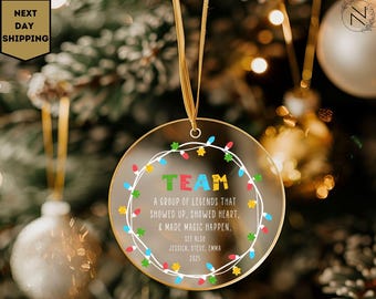 May include: A clear, round Christmas ornament with the word "TEAM" in colorful letters. The ornament has a string of colorful lights around the edge and text that reads "A group of legends that showed up, showed heart, & made magic happen."