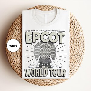 A white t-shirt with a graphic design featuring the EPCOT World Tour logo and a large globe, placed on a woven placemat.