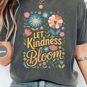 a woman wearing a t - shirt that says let kindness bloom