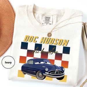 a white t-shirt with a graphic design of a blue car and the text "DOC HUDSON" printed on it.