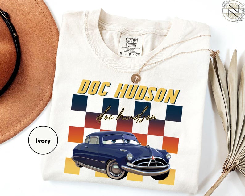 a white t-shirt with a graphic design of a blue car and the text "DOC HUDSON" printed on it.