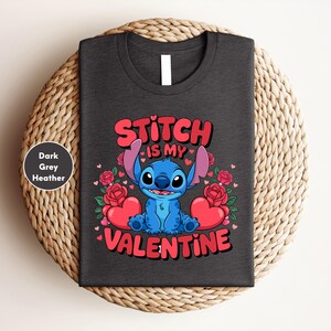 A black t-shirt with a graphic design featuring a blue character, likely Stitch, surrounded by hearts and roses, with the text "Stitch is my Valentine" printed on it.
