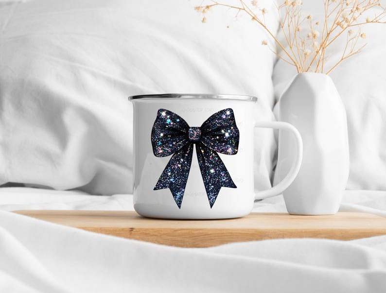 May include: White enamel mug with a black glitter bow design. The mug has a handle and a white background.