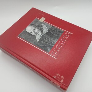 May include: A red hardcover book titled "The Complete Works of Shakespeare." The cover features a portrait of William Shakespeare in a black and white illustration. The book is rectangular and appears to be in good condition.