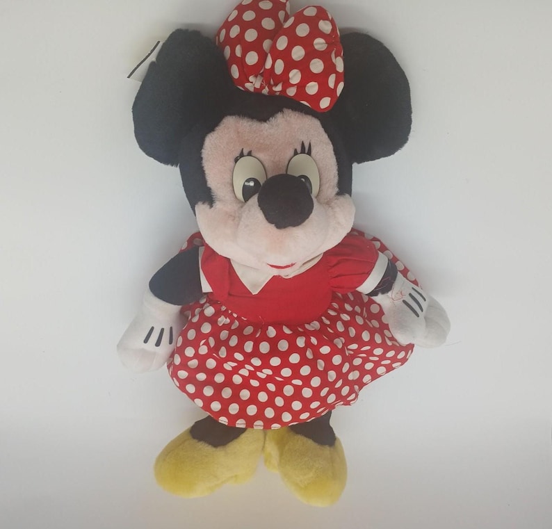 May include: A plush Minnie Mouse doll. The doll has black ears, a red and white polka dot bow, and a red dress with white polka dots. The doll's shoes are yellow, and its gloves are white.