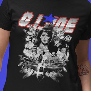 以下が含まれることがあります： 白いグレーのグラフィックが施された黒いTシャツ。グラフィックには、人々や飛行機が描かれており、赤い文字と青い文字で「G.I. JOE」と書いてあり、青い星が描かれている。