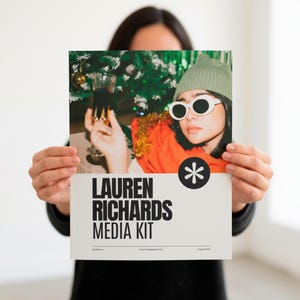 Puede incluir: Una persona sosteniendo un kit de medios con el texto "LAUREN RICHARDS MEDIA KIT". El kit presenta una foto de una persona con gafas de sol y un gorro. La foto tiene un fondo festivo con un árbol de Navidad.