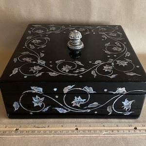 May include: Black lacquered box with silver floral and vine design. The box has a silver knob on top and is approximately 10 inches long. The box is decorated with inlaid mother-of-pearl accents.