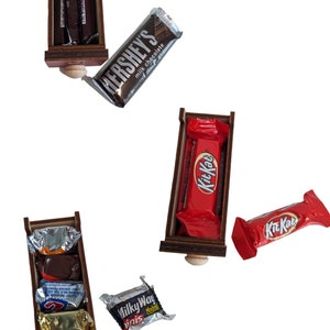 May include: Four wooden drawers with different chocolate bars inside. The drawers are open and the chocolate bars are visible. The chocolate bars are Hershey's milk chocolate, Kit Kat, Milky Way, and a variety pack of chocolate bars.