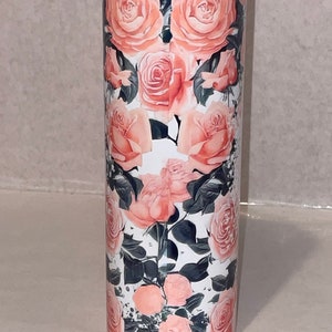 Puede incluir: Un vaso de acero inoxidable con un dise&ntilde;o floral rosa. El vaso tiene un fondo blanco con rosas rosas y hojas verdes.