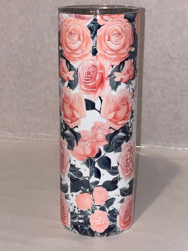 Puede incluir: Un vaso de acero inoxidable con un dise&ntilde;o floral rosa. El vaso tiene un fondo blanco con rosas rosas y hojas verdes.