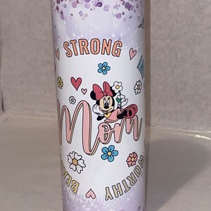 May include: A white tumbler with a purple glitter background. It features a cartoon image of Minnie Mouse with the word "Mom" in pink letters. The words "Strong, Worthy, Beautiful" are written around the image in gold letters.