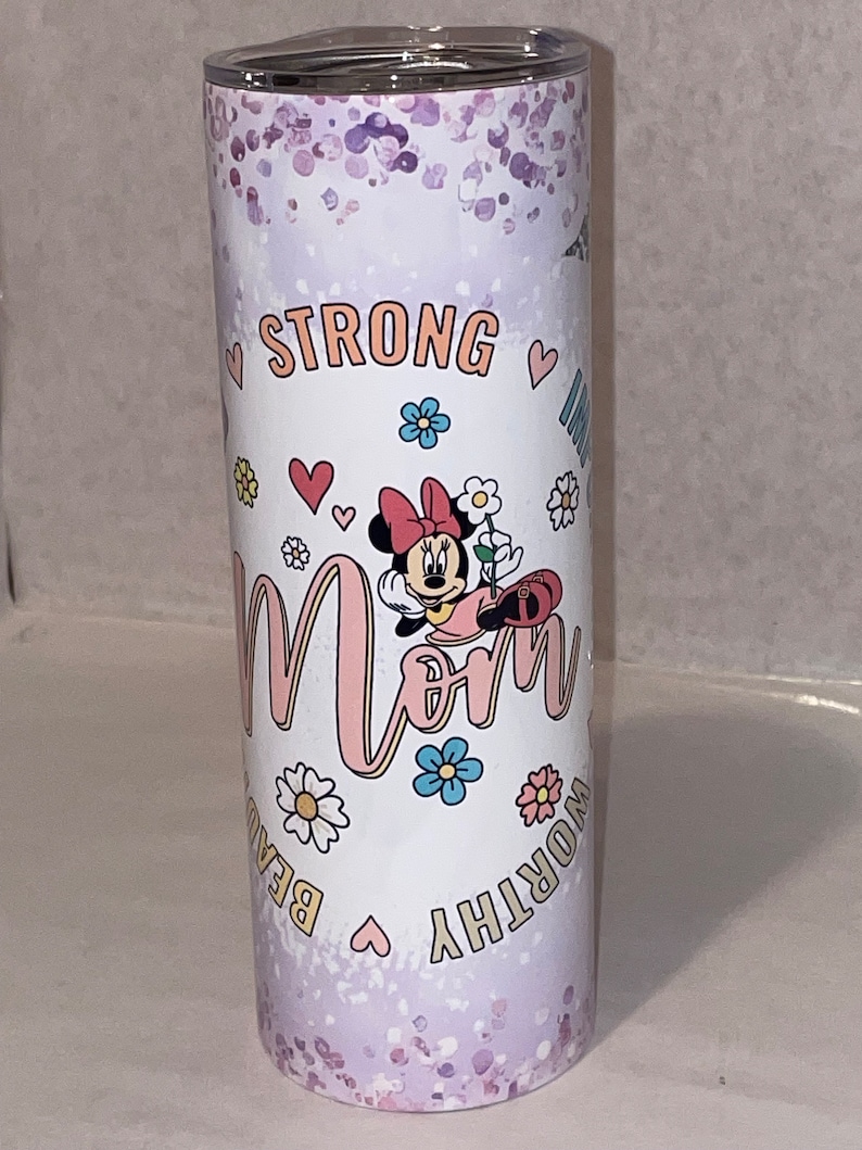May include: A white tumbler with a purple glitter background. It features a cartoon image of Minnie Mouse with the word "Mom" in pink letters. The words "Strong, Worthy, Beautiful" are written around the image in gold letters.