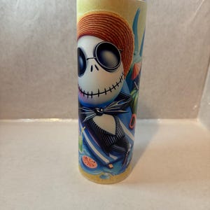 K&ouml;nnte beinhalten: Ein Edelstahlbecher mit einer farbenfrohen Illustration von Jack Skellington aus The Nightmare Before Christmas. Jack ist mit Sonnenbrille und Strohhut dargestellt, wie er sich an einem Strand mit einem Cocktail entspannt. Der Becher ist zylindrisch und hat einen silbernen Deckel.