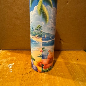 May include: A stainless steel tumbler with a tropical beach scene design. The design features palm trees, a beach, ocean waves, and colorful hibiscus flowers.
