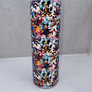 May include: A cylindrical tumbler featuring a repeating pattern of Mickey Mouse dressed as various superheroes, including Wolverine, Thor, Captain America, and Spider-Man, set against a white background with colorful paint splatter accents.