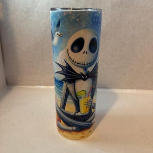 May include: A stainless steel tumbler with a colorful image of Jack Skellington from The Nightmare Before Christmas enjoying a tropical drink on a beach. The background is a blue sky with clouds and a seagull.