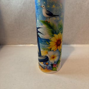 May include: A white stainless steel tumbler with a colorful design featuring a beach scene with a seagull, palm trees, flowers, and a blue ocean.