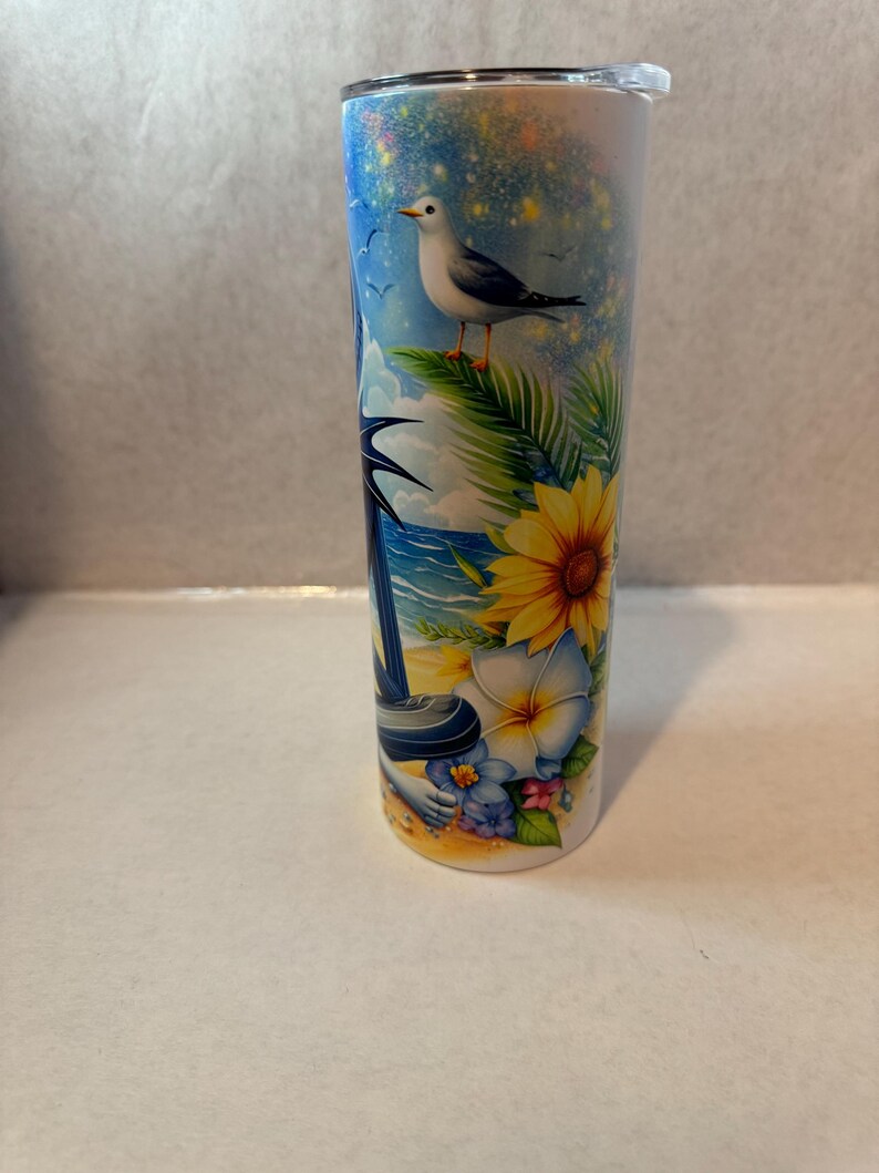 May include: A white stainless steel tumbler with a colorful design featuring a beach scene with a seagull, palm trees, flowers, and a blue ocean.