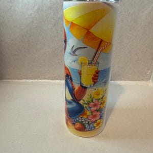 May include: A stainless steel tumbler with a colorful design featuring a cartoon superhero relaxing on a beach with a glass of lemonade under an umbrella.