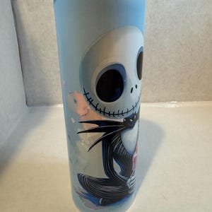 Może przedstawiać: Kubek ze stali nierdzewnej z Jackiem Skellingtonem z filmu Miasteczko Halloween. Kubek ma jasnoniebieskie tło z kolorową ilustracją Jacka w jego charakterystycznym czarno-białym stroju.