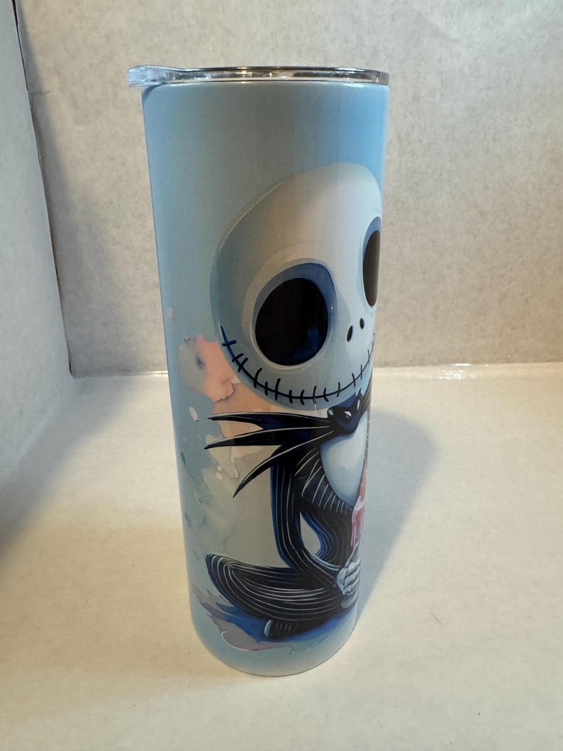 Może przedstawiać: Kubek ze stali nierdzewnej z Jackiem Skellingtonem z filmu Miasteczko Halloween. Kubek ma jasnoniebieskie tło z kolorową ilustracją Jacka w jego charakterystycznym czarno-białym stroju.