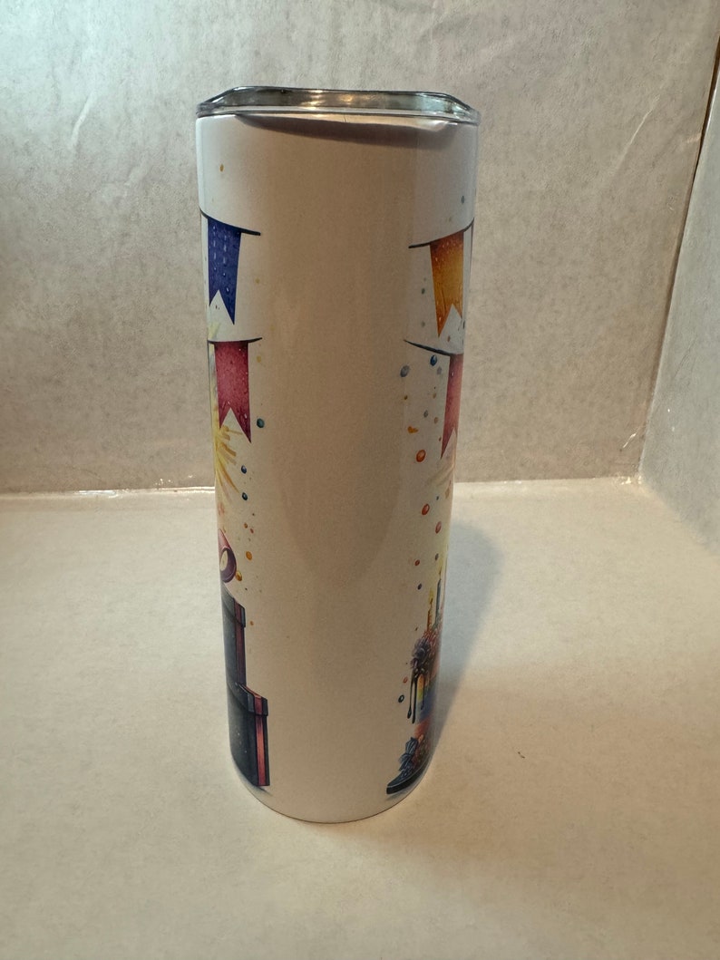 Może przedstawiać: Biały kubek ze stali nierdzewnej z wzorem tortu urodzinowego. Tort jest ozdobiony kolorowymi posypkami, świeczkami i banerem. Kubek idealnie nadaje się do przechowywania gorących lub zimnych napoj&oacute;w.