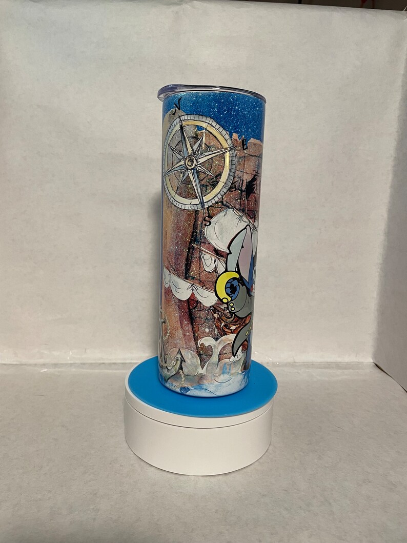 May include: A blue and white tumbler with a nautical theme. The tumbler features a compass, a ship, and a cartoon animal. The tumbler is on a blue and white stand.