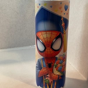 Pode incluir: Um copo de a&ccedil;o inoxid&aacute;vel branco com uma imagem colorida de um Homem-Aranha de desenho animado vestindo um chap&eacute;u de formatura e uma beca. Ele est&aacute; segurando um buqu&ecirc; de flores. O fundo &eacute; amarelo claro com cora&ccedil;&otilde;es e estrelas azuis.