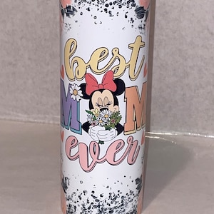 Puede incluir: Un vaso blanco con un fondo moteado en blanco y negro. El vaso presenta una imagen de dibujos animados de Minnie Mouse sosteniendo un ramo de flores. El texto "best mom ever" est&aacute; escrito en letras de colores alrededor de la imagen.